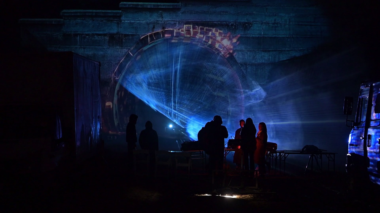 A stone railway tunnel portal in Tbilisi covered in a projection mapping of coloured tiles, with a hologram of light appearing in the tunnel mouth