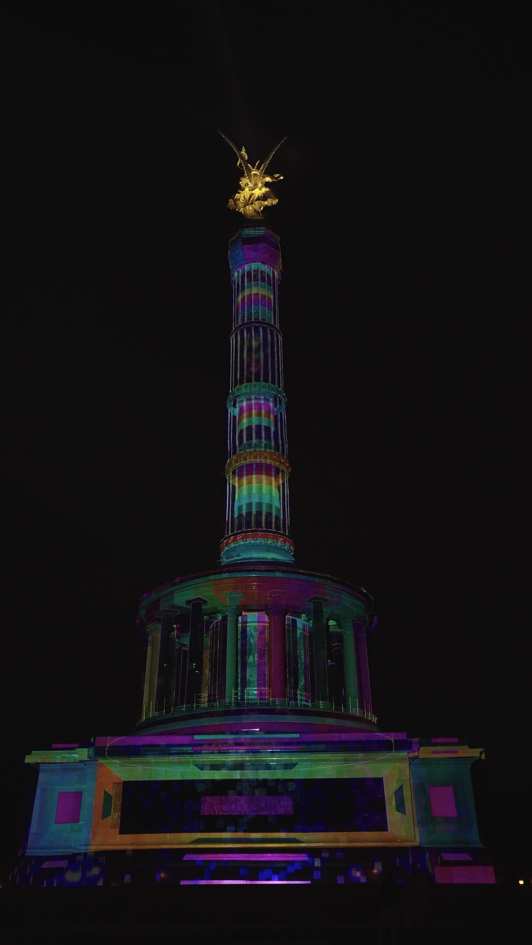 The Berlin Victory Column wrapped in a rainbow-coloured 360-degree projection mapping at night, filmed from below