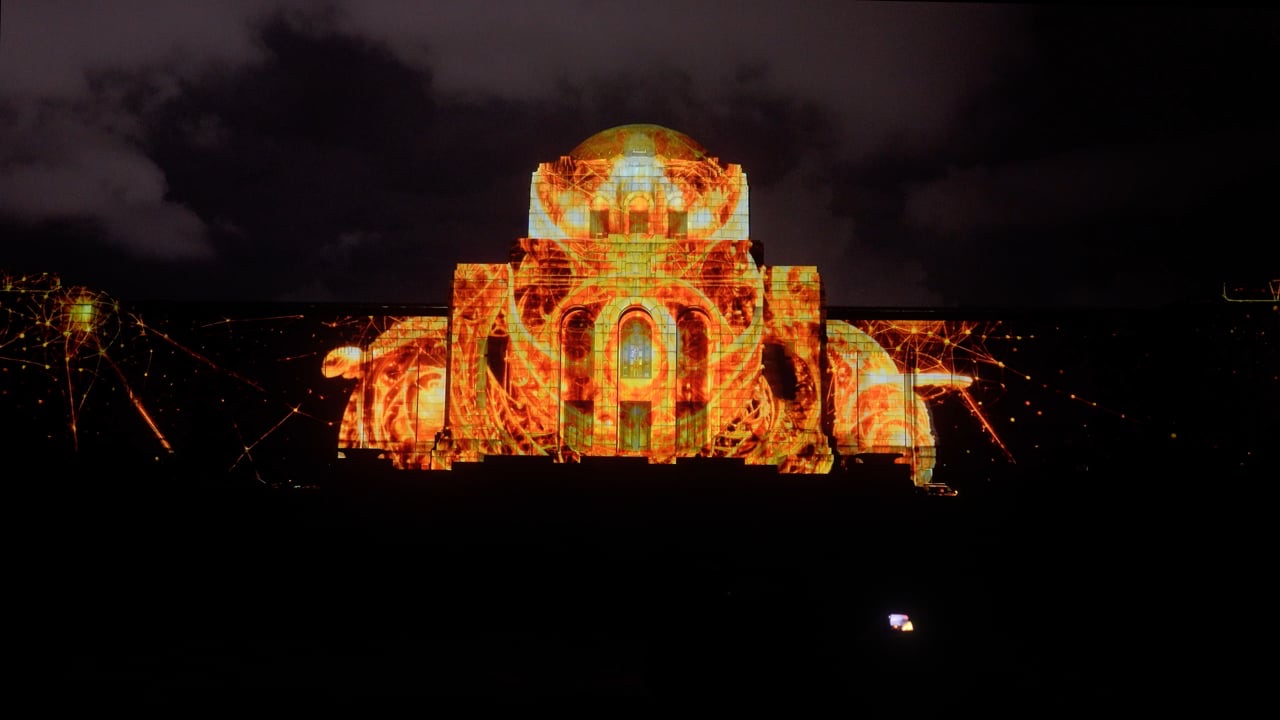 A façade in Tokyo lit by a projection mapping in which a giant face emerges from golden light